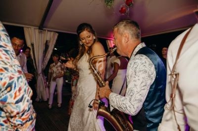 Une femme en robe blanche danse avec un saxophoniste jouant lors d'une soirée festive en intérieur.