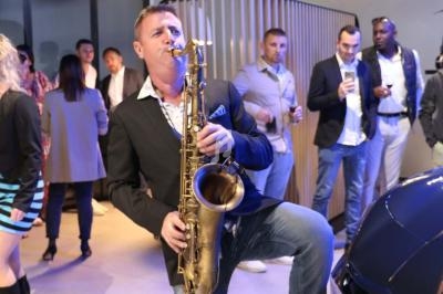 Un musicien joue du saxophone lors d'un événement, entouré de personnes debout dans un espace intérieur.