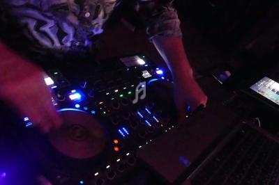 Un DJ mixe de la musique sur une table de mixage éclairée, avec un ordinateur portable à proximité.