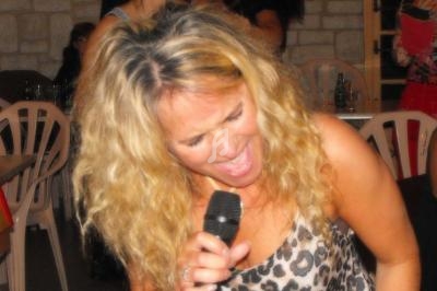 Femme blonde chantant avec énergie dans un micro lors d'un événement en intérieur.