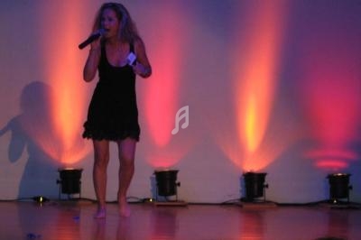 Une femme chante pieds nus sur une scène éclairée par des projecteurs aux teintes orange et violette.