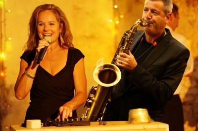 Une chanteuse et un saxophoniste jouent de la musique dans un décor chaleureux avec des lumières tamisées.