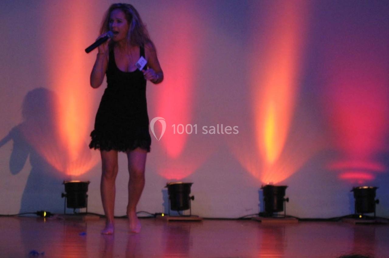 Une femme chante pieds nus sur une scène éclairée par des projecteurs aux teintes orange et violette.