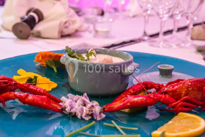 Assiette de présentation avec écrevisses, fleurs comestibles, citron et une cocotte contenant une préparation culinaire.