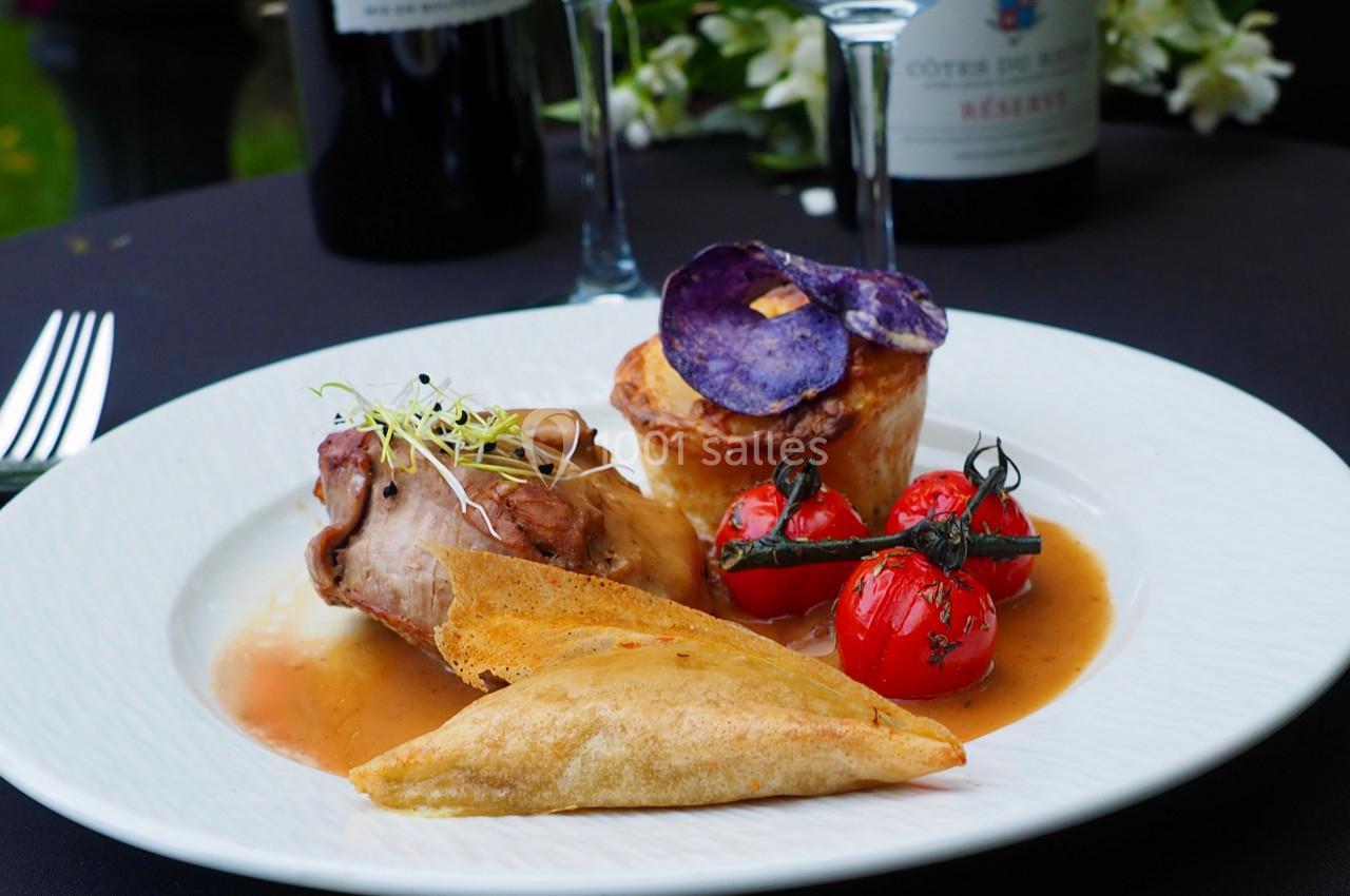 Assiette gastronomique avec viande, légumes, croustillant et sauce, accompagnée de verres et bouteilles de vin en arrière…