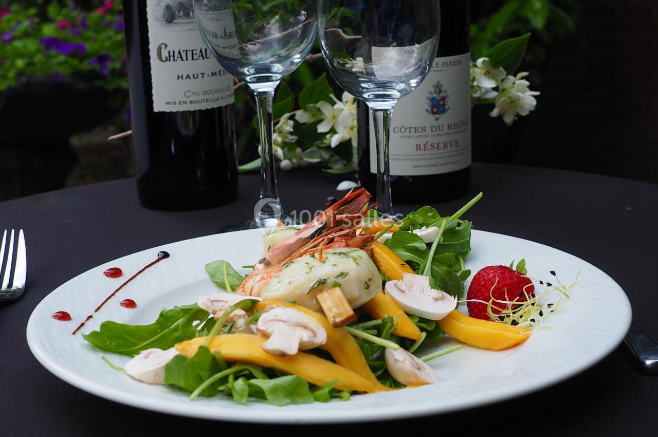 Assiette de salade composée avec crevettes, mangue, champignons et verdure, servie sur une table avec des verres et…