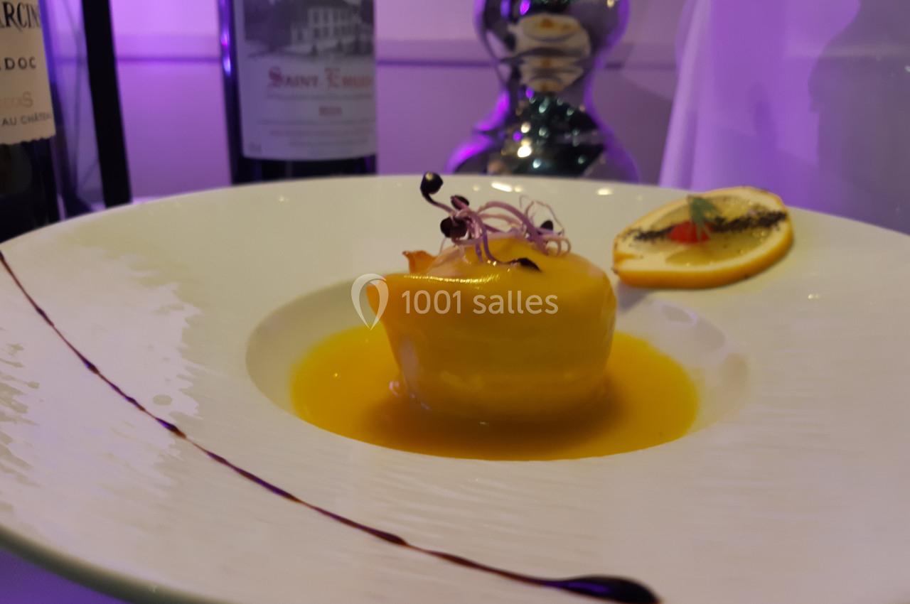 Plat gastronomique avec un dessert jaune brillant, nappé de sauce, décoré de pousses et accompagné d'une tranche d'orange.
