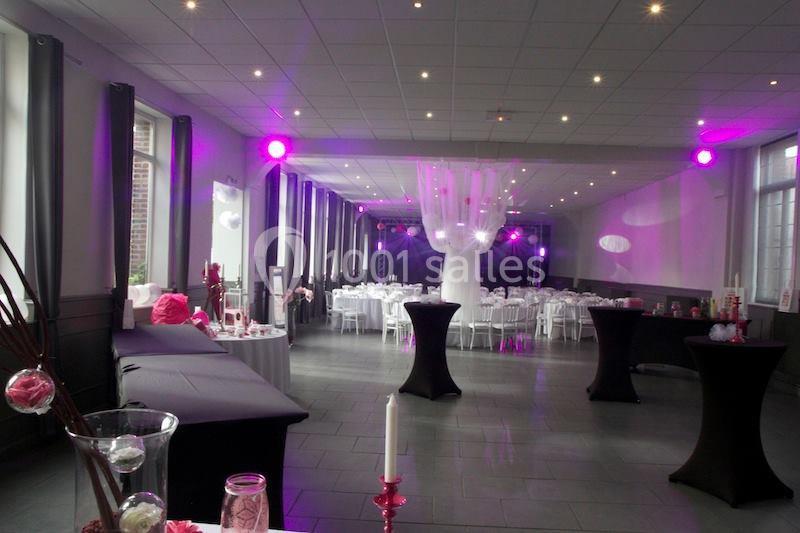 Salle de réception décorée avec des tables rondes, nappes blanches et éclairage rose tamisé.