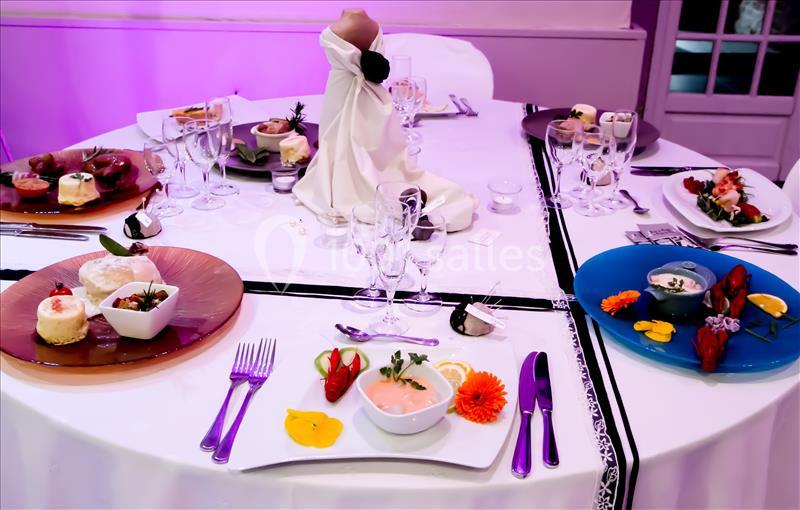 Table dressée avec des assiettes gastronomiques colorées, couverts disposés et décoration élégante sous éclairage violet.