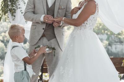 Femme assise, vêtue d'une robe blanche fluide, posant avec une expression sereine sur fond neutre.