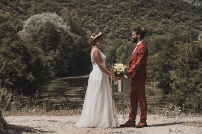 Femme assise, vêtue d'une robe blanche fluide, posant avec une expression sereine sur fond neutre.