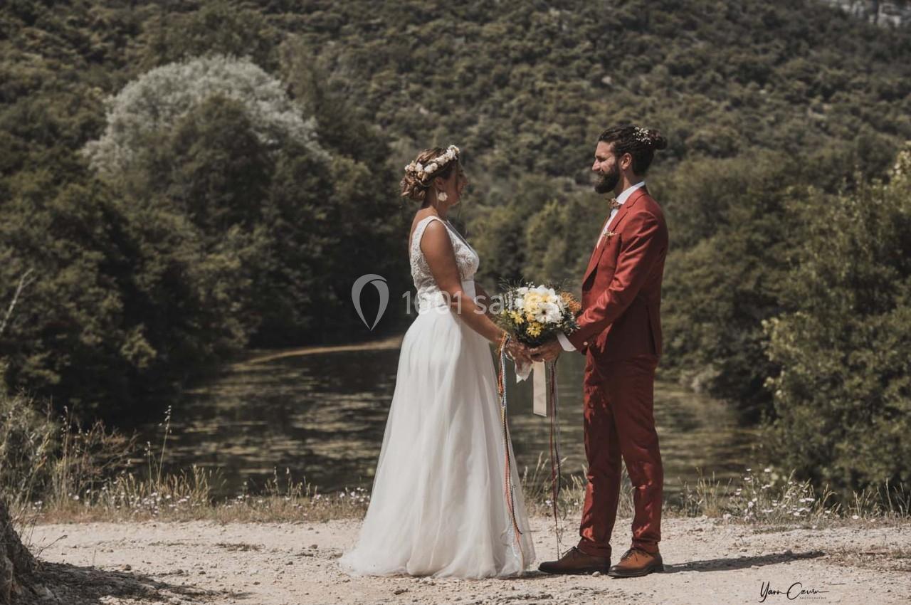 Un couple en tenue de mariage se tient face à face près d'un plan d'eau entouré de végétation.