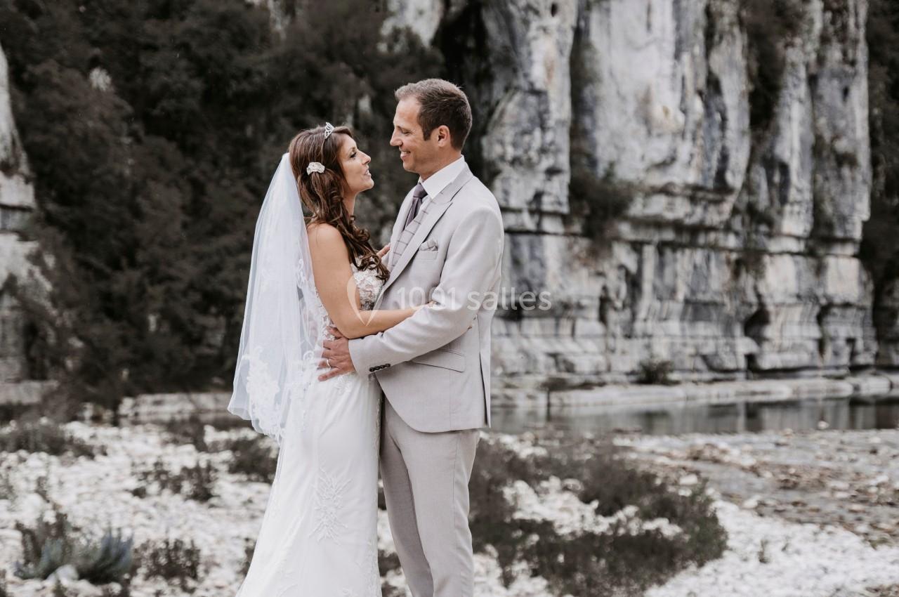 Un couple en tenue de mariage se tient face à face près de falaises rocheuses.