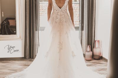 Femme assise, vêtue d'une robe blanche fluide, posant avec une expression sereine sur fond neutre.