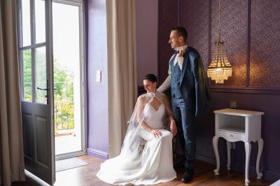 Femme assise, vêtue d'une robe blanche fluide, posant avec une expression sereine sur fond neutre.