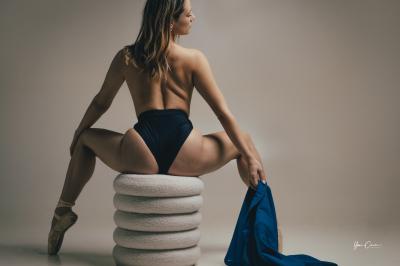 Femme assise, vêtue d'une robe blanche fluide, posant avec une expression sereine sur fond neutre.