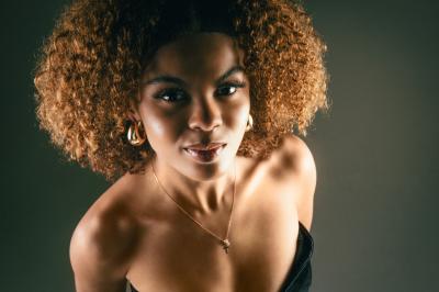 Femme assise, vêtue d'une robe blanche fluide, posant avec une expression sereine sur fond neutre.