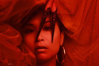 Femme assise, vêtue d'une robe blanche fluide, posant avec une expression sereine sur fond neutre.