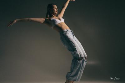 Femme assise, vêtue d'une robe blanche fluide, posant avec une expression sereine sur fond neutre.