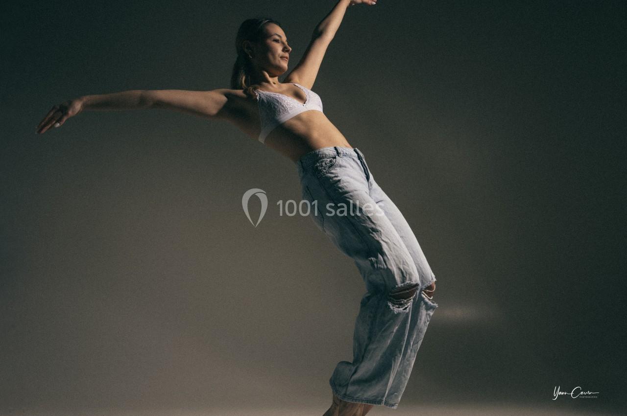 Une femme en mouvement effectue une pose de danse contemporaine dans un studio sombre.