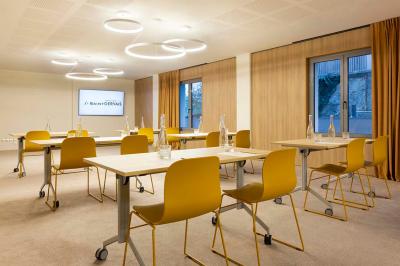 Façade d'un bâtiment éclairé la nuit, entouré d'un jardin avec des arbres, des chaises et des tables en extérieur.