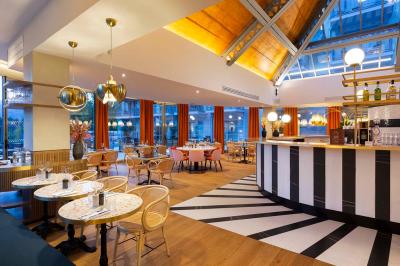 Façade d'un bâtiment éclairé la nuit, entouré d'un jardin avec des arbres, des chaises et des tables en extérieur.