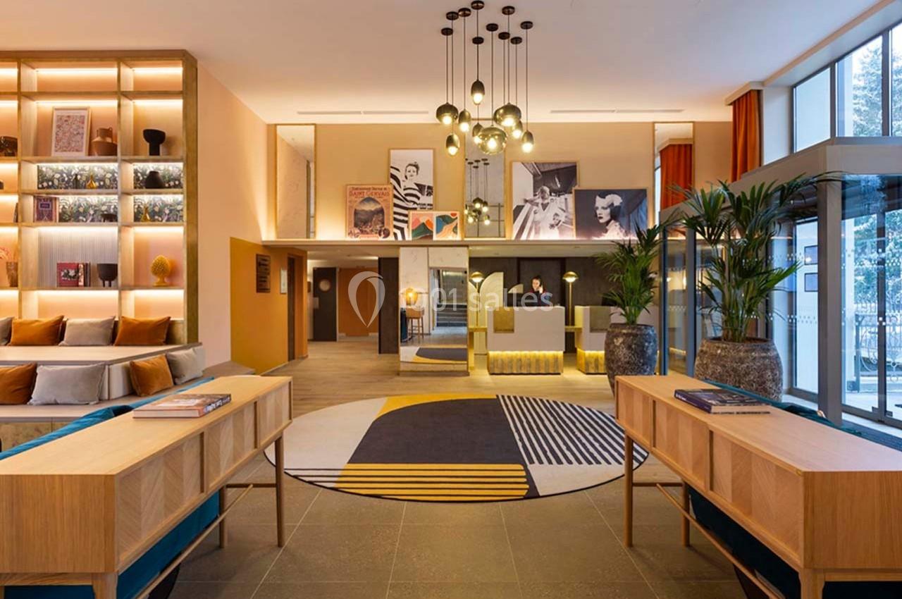 Hall d'entrée moderne avec mobilier en bois, tapis géométrique coloré, luminaires suspendus et plantes décoratives.