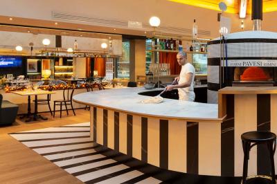 Façade d'un bâtiment éclairé la nuit, entouré d'un jardin avec des arbres, des chaises et des tables en extérieur.