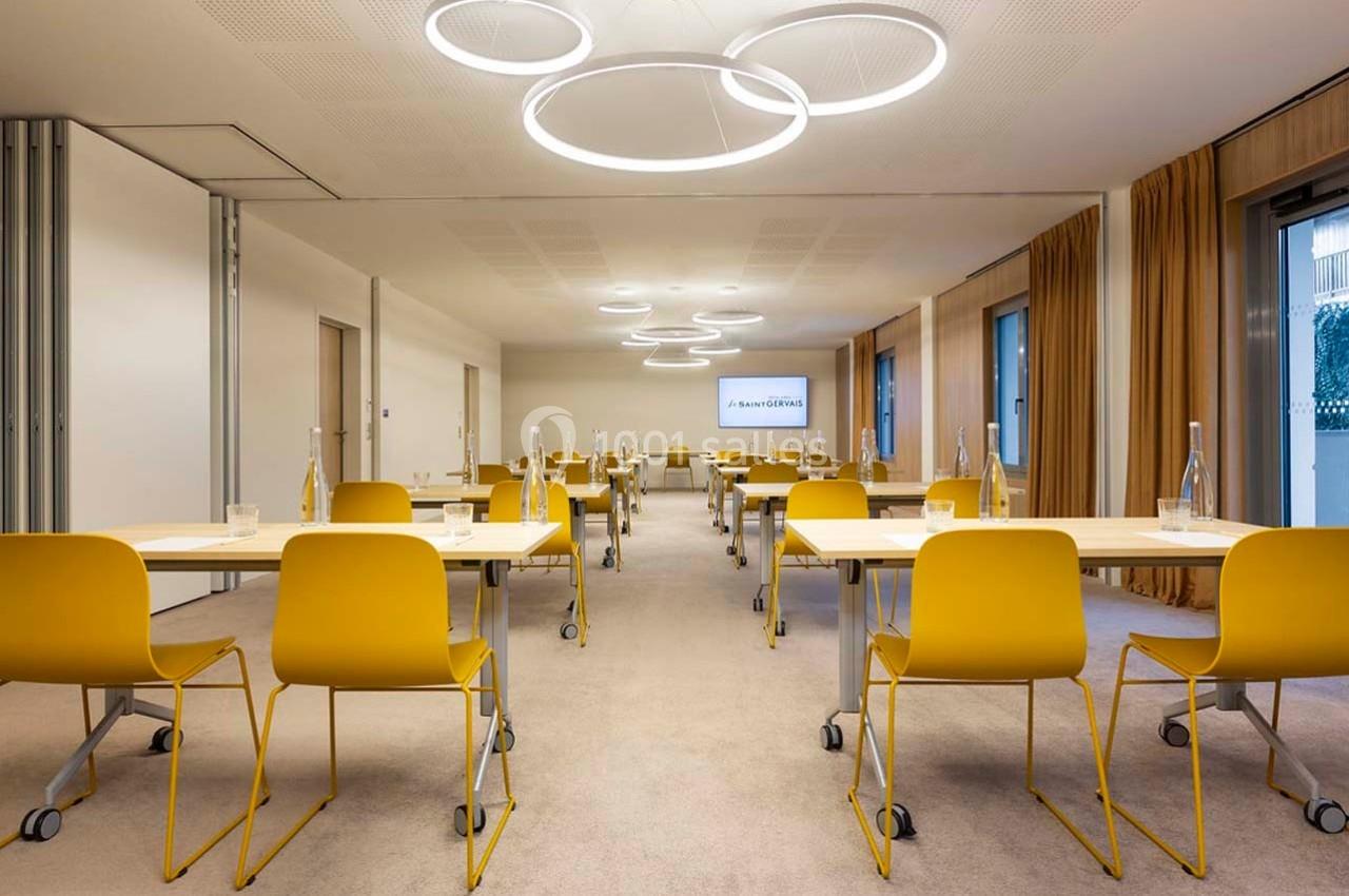 Salle de réunion lumineuse avec des chaises jaunes, des tables en bois clair et des luminaires circulaires suspendus.