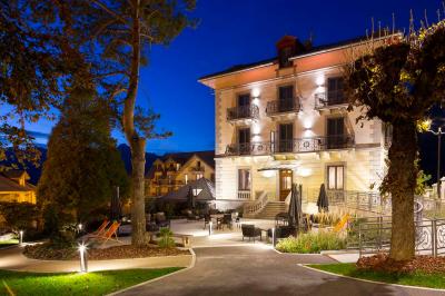 Façade d'un bâtiment éclairé la nuit, entouré d'un jardin avec des arbres, des chaises et des tables en extérieur.