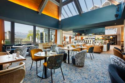 Façade d'un bâtiment éclairé la nuit, entouré d'un jardin avec des arbres, des chaises et des tables en extérieur.