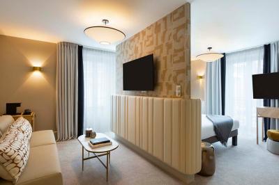 Façade d'un bâtiment éclairé la nuit, entouré d'un jardin avec des arbres, des chaises et des tables en extérieur.