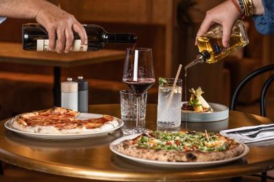 Façade d'un bâtiment éclairé la nuit, entouré d'un jardin avec des arbres, des chaises et des tables en extérieur.