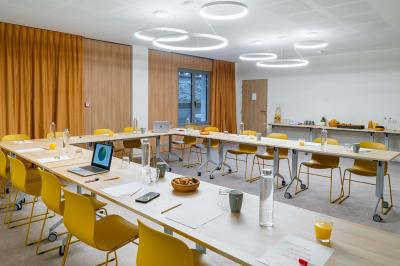 Façade d'un bâtiment éclairé la nuit, entouré d'un jardin avec des arbres, des chaises et des tables en extérieur.