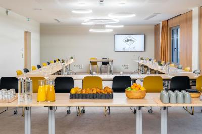 Façade d'un bâtiment éclairé la nuit, entouré d'un jardin avec des arbres, des chaises et des tables en extérieur.