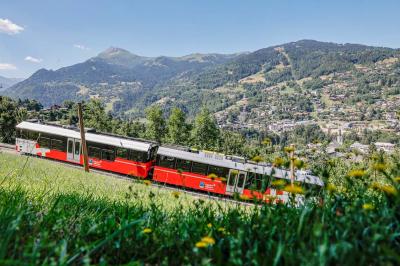 Façade d'un bâtiment éclairé la nuit, entouré d'un jardin avec des arbres, des chaises et des tables en extérieur.
