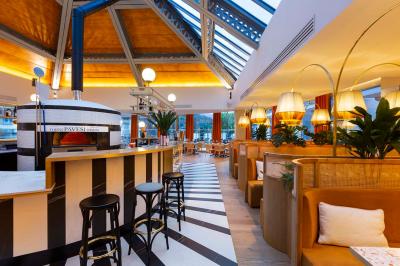 Façade d'un bâtiment éclairé la nuit, entouré d'un jardin avec des arbres, des chaises et des tables en extérieur.