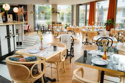 Façade d'un bâtiment éclairé la nuit, entouré d'un jardin avec des arbres, des chaises et des tables en extérieur.