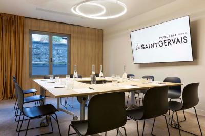 Façade d'un bâtiment éclairé la nuit, entouré d'un jardin avec des arbres, des chaises et des tables en extérieur.