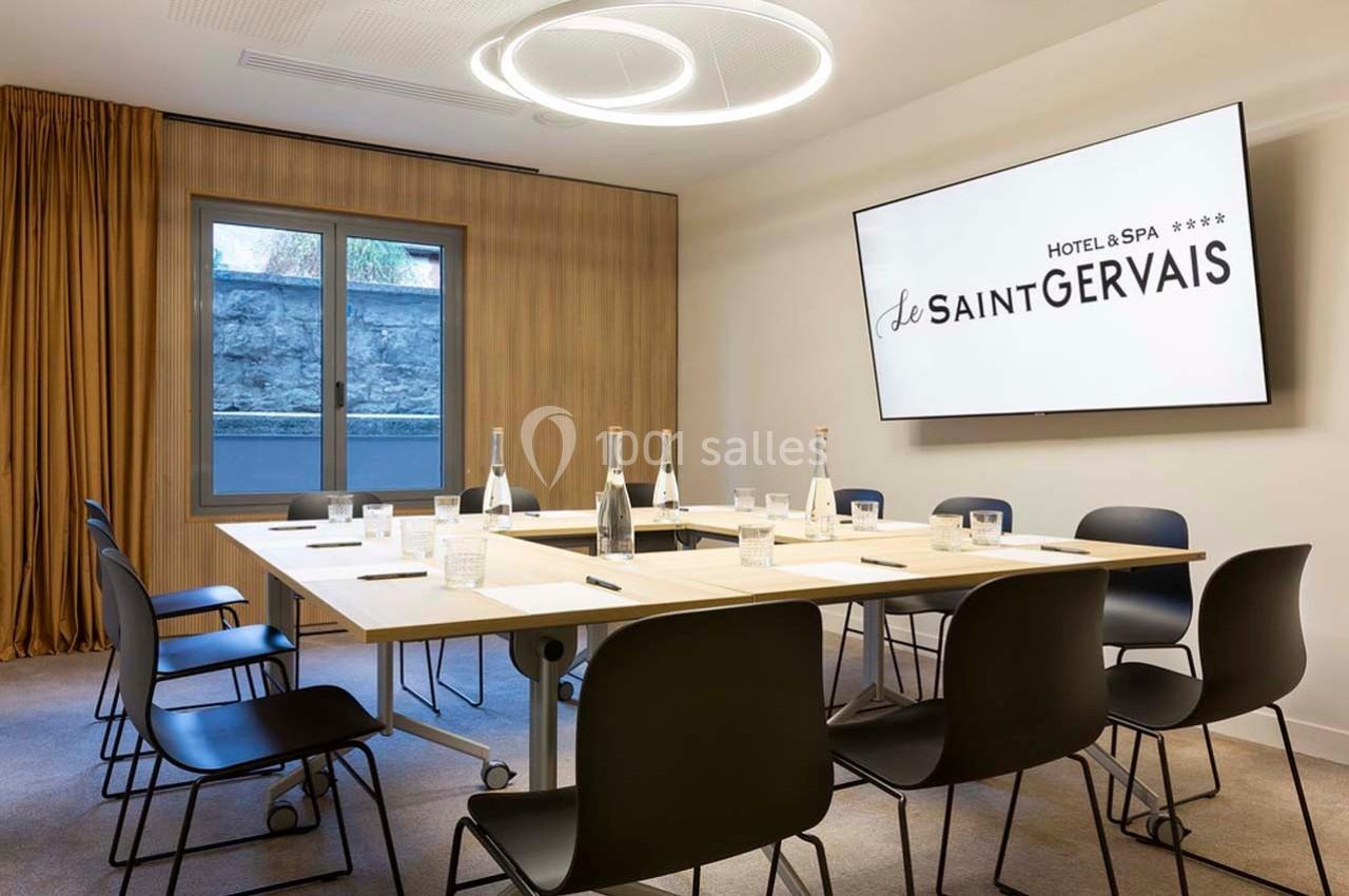 Salle de réunion moderne avec table rectangulaire, chaises noires, écran mural et bouteilles d'eau disposées.