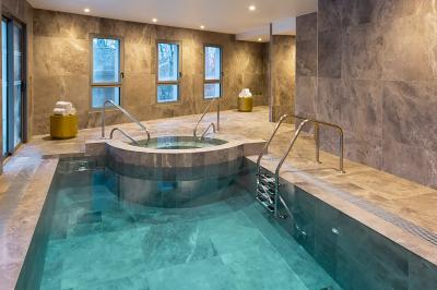 Façade d'un bâtiment éclairé la nuit, entouré d'un jardin avec des arbres, des chaises et des tables en extérieur.