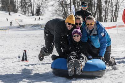 Façade d'un bâtiment éclairé la nuit, entouré d'un jardin avec des arbres, des chaises et des tables en extérieur.