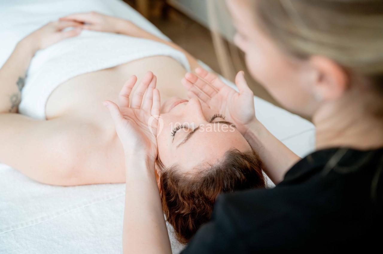 Une femme reçoit un massage du visage allongée sur une table recouverte d'une serviette blanche.