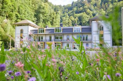 Façade d'un bâtiment éclairé la nuit, entouré d'un jardin avec des arbres, des chaises et des tables en extérieur.