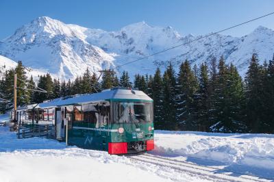 Façade d'un bâtiment éclairé la nuit, entouré d'un jardin avec des arbres, des chaises et des tables en extérieur.
