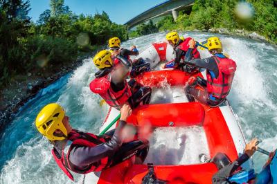 Façade d'un bâtiment éclairé la nuit, entouré d'un jardin avec des arbres, des chaises et des tables en extérieur.