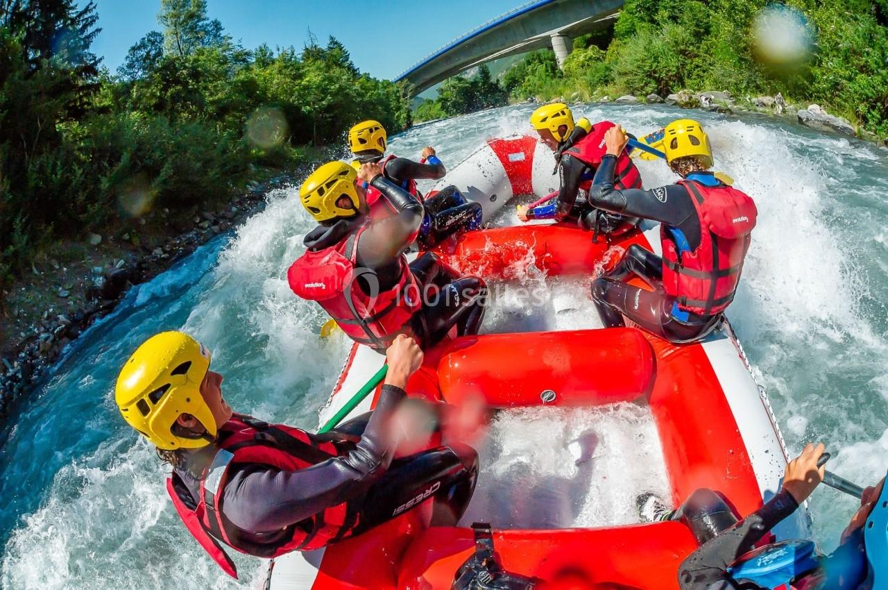 Des personnes en combinaison et casque jaune pratiquent le rafting sur une rivière rapide entourée de végétation.