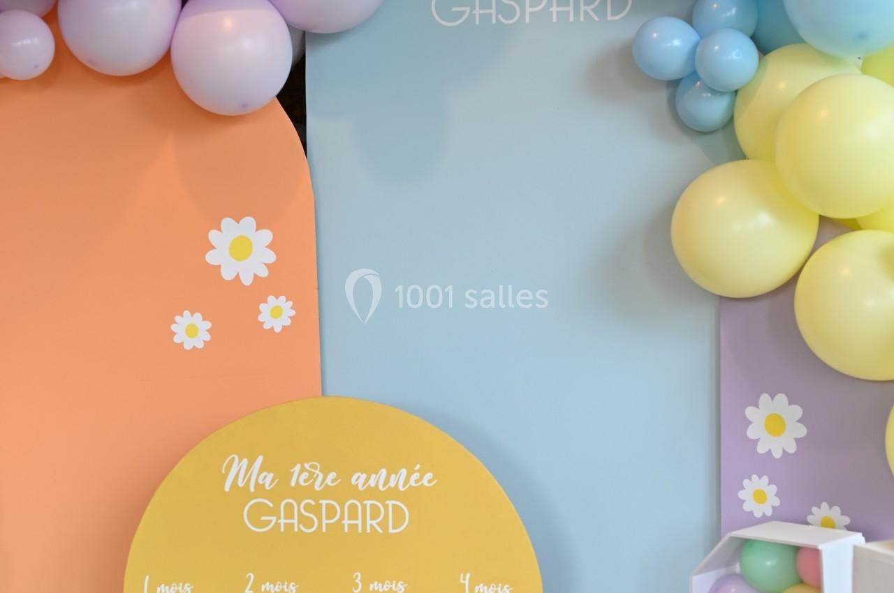 Décoration d'anniversaire colorée avec des ballons pastel et un panneau montrant des photos mensuelles d'un enfant.