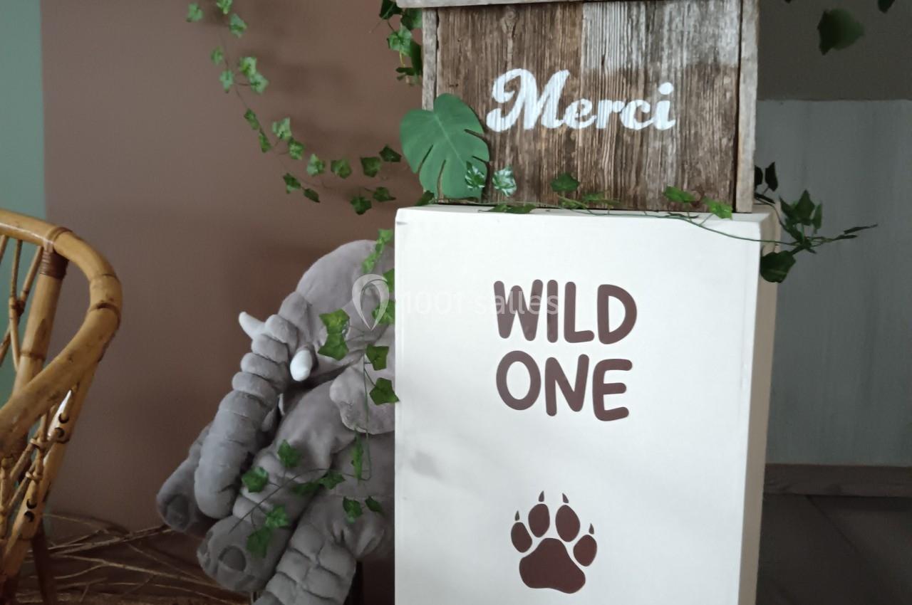 Décoration sur le thème de la jungle avec ballons colorés, feuillage, panneau ’Merci’ et mention ’Wild One’ sur une boîte.