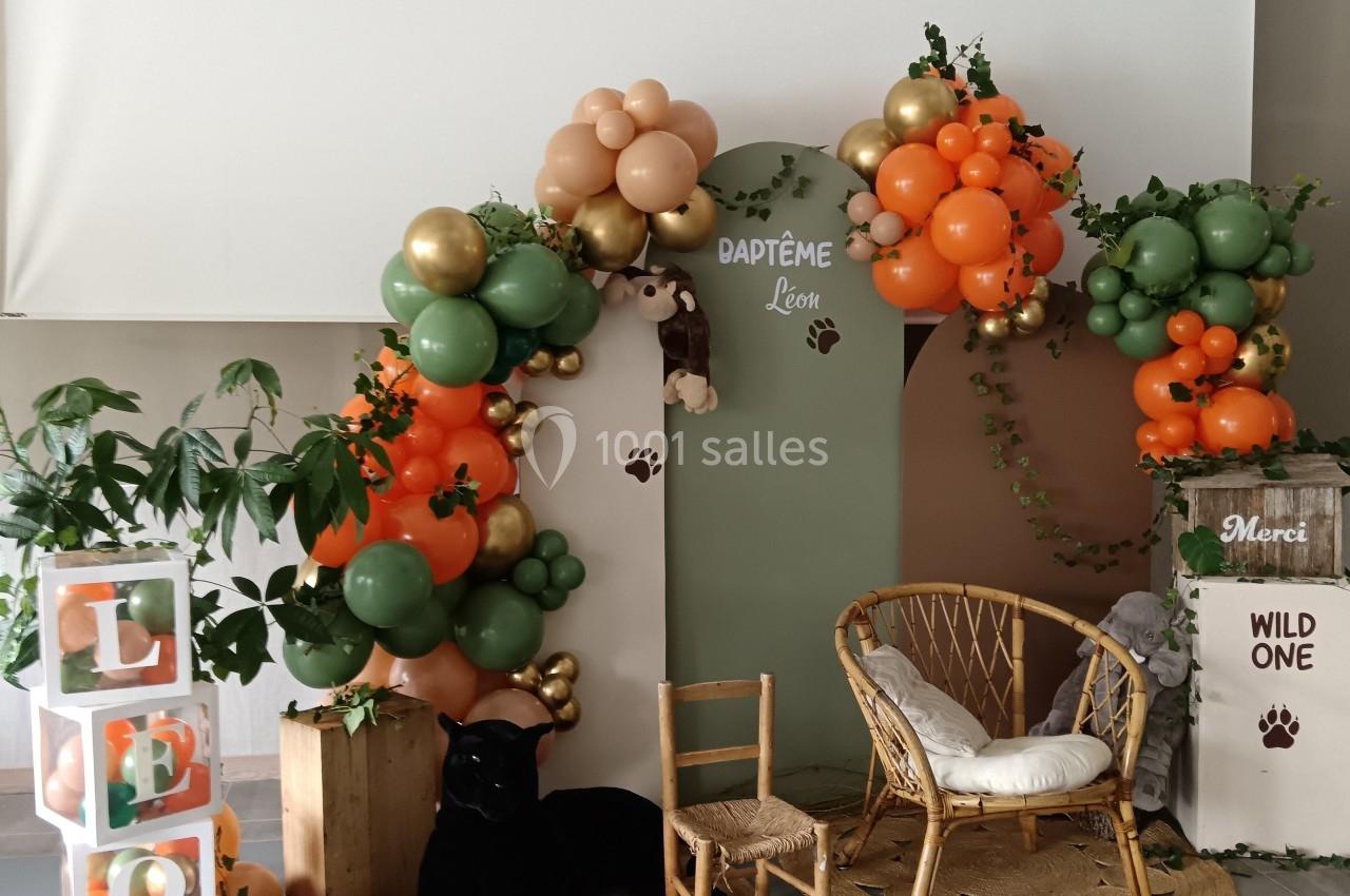 Décoration de baptême sur le thème de la jungle avec ballons colorés, fauteuil en rotin et éléments naturels.